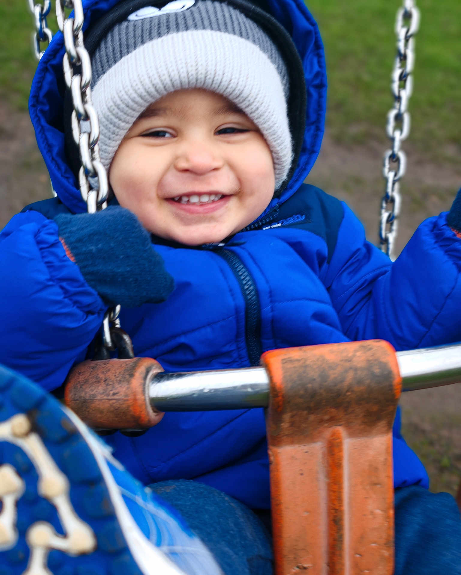 Kevin is registered to the contest to win money with this photo: blue_jacket, chains, child, cold_weather, cute, face, fun, gloves, happy, jacket, knit_hat, outdoor, park, person, playground, seat, smiling, swing, toddler, winter