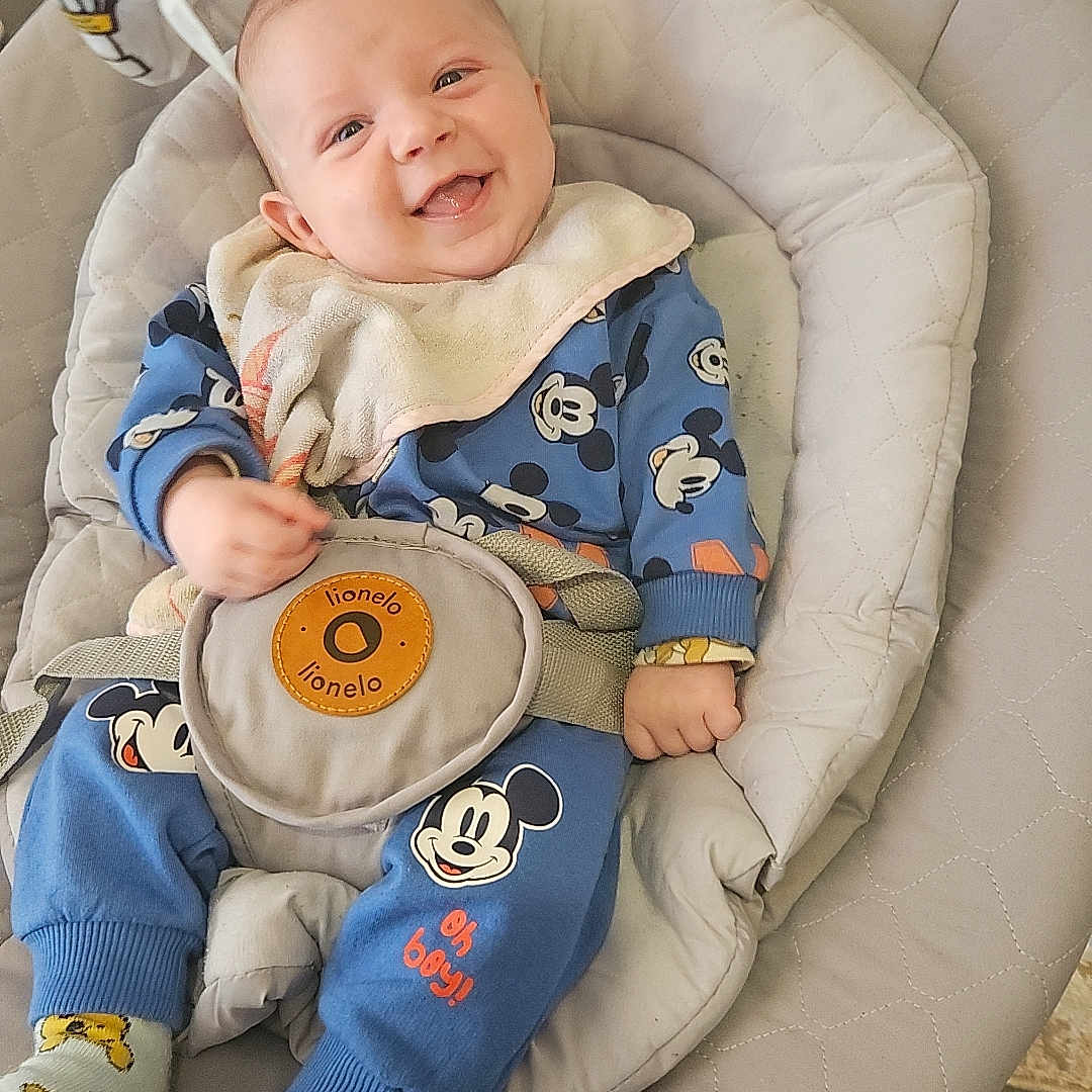 Gabriel a rejoint le concours — aidez-le/la à gagner de superbes lots ! baby, baby_rocker, blue_clothing, child, comfortable, cute, face, footwear, happy, home, indoor, infant, mickey_mouse, person, playful, seat_belt, smiling, socks, toddler, toy