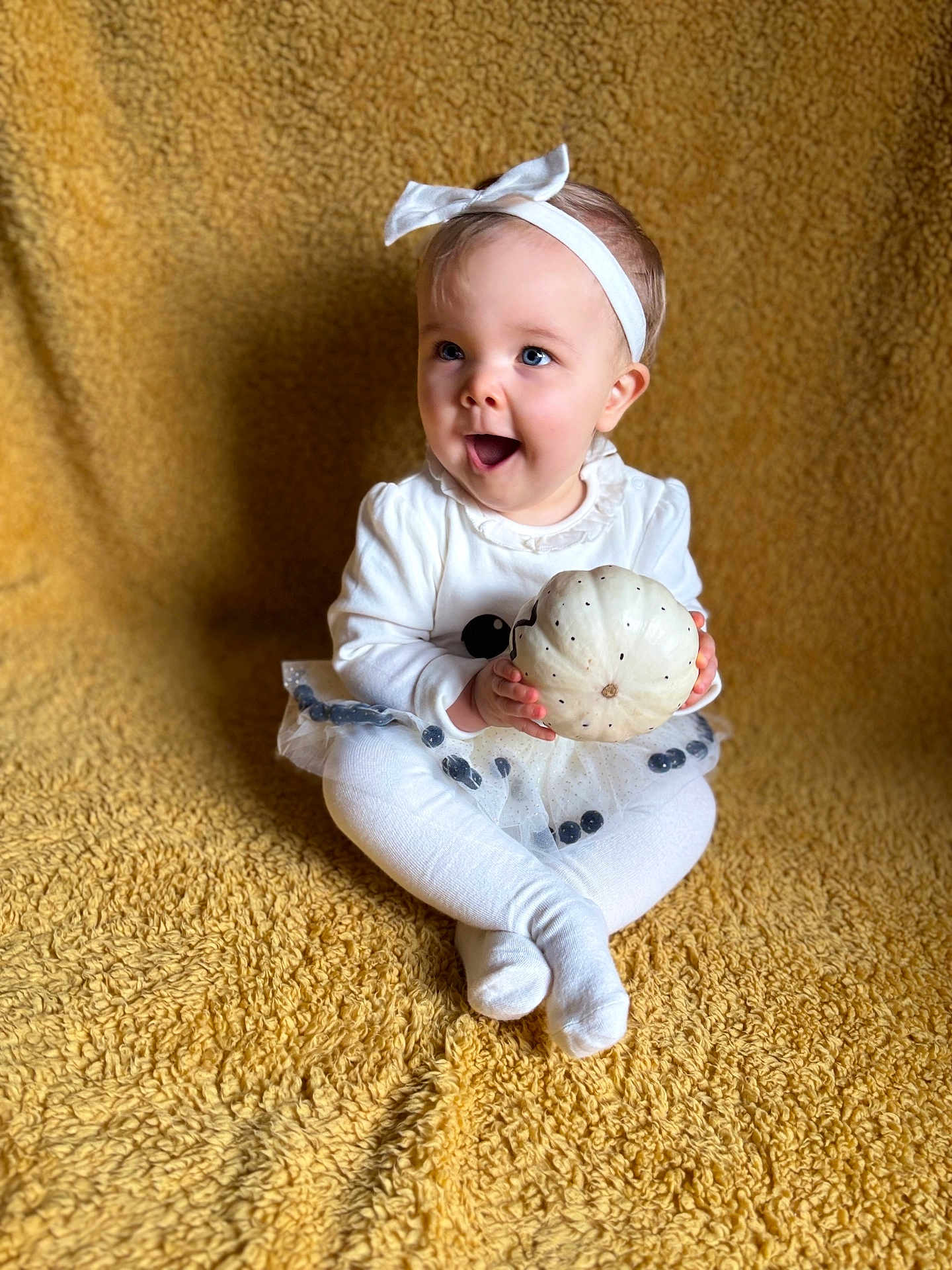 Winnie-Kay is registered to the contest to win money with this photo: baby, bow, child, cute, expression, festive, girl, happy, headband, holiday, indoors, playful, portrait, pumpkin, sitting, smiling, soft_texture, toddler, white_clothing, yellow_blanket