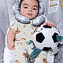 baby, infant, plush_toy, soccer_ball, baby_seat, cushion, clothing, cookie_pattern, footwear, socks, head_support, indoor, child, cute, soft_toy, person, comfort, relaxing, portrait, toddler