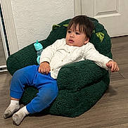 Joel Hernandez is registered to the contest to win money with this photo: toddler, child, indoor, plush_chair, green_chair, white_shirt, blue_pants, socks, flooring, wood_floor, relaxed, furniture, face, hair, bottle, toy, ear_shape, expression, person, casual