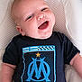 baby, smiling, infant, tshirt, logo, blue, white, cushion, happy, portrait, child, cute, laying, apparel, clothing, face, person, indoors, young, joyful
