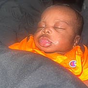 Kamari is registered to the contest to win money with this photo: baby, blanket, child, closeup, cozy, cute, face, head, indoors, infant, orange_shirt, peaceful, person, portrait, resting, skin, sleeping, soft_light, wearing, young