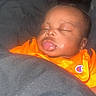 baby, blanket, child, closeup, cozy, cute, face, head, indoors, infant, orange_shirt, peaceful, person, portrait, resting, skin, sleeping, soft_light, wearing, young