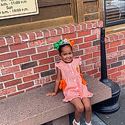 Heaven is registered to the contest to win money with this photo: child, girl, smiling, bench, brick_wall, wooden_wall, outdoor, dress, sandals, hair_bow, tiara, concrete, sidewalk, window, reflection, lamp_post, happy, portrait, cute, fashion