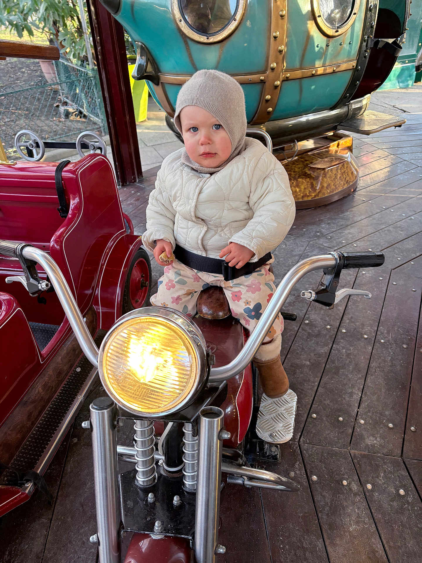 Marlo a rejoint le concours — aidez-le/la à gagner de superbes lots ! toddler, child, motorcycle, headlight, jacket, hat, snack, ride, amusement_park, floor, wooden_floor, boots, seatbelt, outdoor, vehicle, handlebars, play, portrait, expression, metal