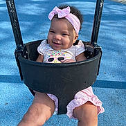 Raniah joined the competition — help win amazing prizes! baby, child, swing, playground, smiling, happy, pink_bow, headband, outdoor, park, infant, portrait, sitting, play_equipment, blue_ground, sunlight, summer, clothing, face, joyful