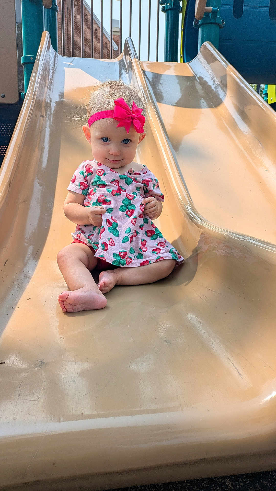 Susanna joined the competition — help win amazing prizes! toddler, child, slide, playground, pink_bow, dress, strawberry_pattern, outdoor, sunlight, barefoot, play, fun, smile, cute, park, equipment, happy, young_child, summer, recreation