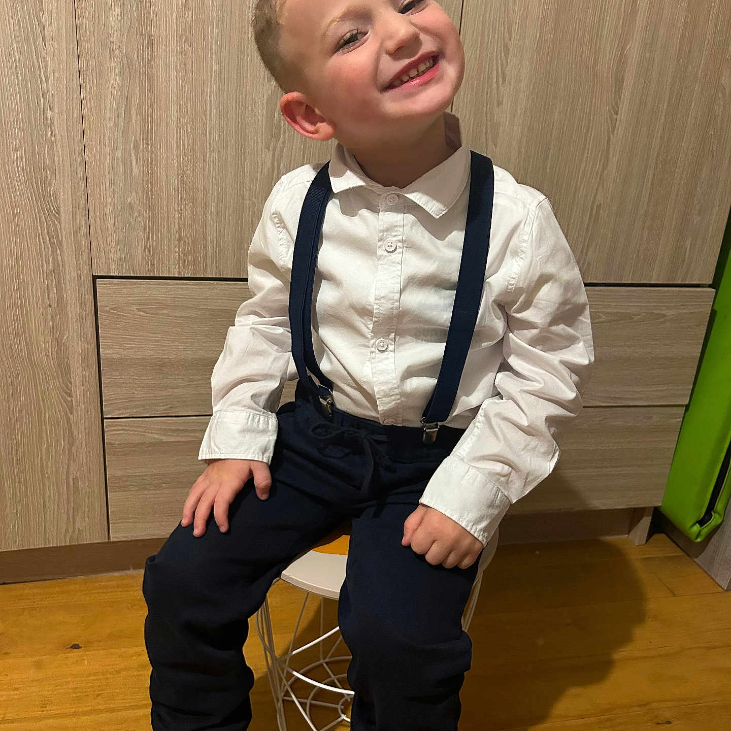 Léo participe au concours pour gagner de l'argent avec cette photo : blue_shoes, boy, casual_clothing, child, fashion, footwear, furniture, happy, indoor, navy_pants, portrait, room, sitting, smile, stool, suspenders, white_shirt, wooden_floor, wooden_wardrobe, young
