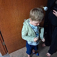 Beckett joined the competition — help win amazing prizes! child, boy, toddler, standing, indoors, doorway, wooden_door, carpet, jacket, hoodie, t_shirt, shorts, sandals, blond_hair, looking_down, adult, phone, toy, home, portrait