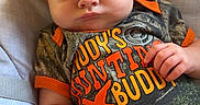 Dean is registered to the contest to win money with this photo: baby, infant, child, portrait, sitting, reclining, serious, pouting, face, smiling, camouflage, outfit, clothing, orange, chair, cushion, indoors, close_up, photography, cute