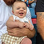 baby, man, beard, smile, people, crowd, spectators, seated, shirt, tattoo, shorts, holding, happy, outdoor, event, portrait, person, face, skin, clothing