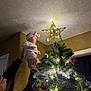 Stella is registered to the contest to win money with this photo: accessories, baby, cap, christmas, christmasdecorations, christmastree, christmastreeornaments, clothing, conifer, face, festival, fir, hat, head, lighting, person, photography, plant, pottedplant, tree