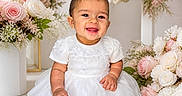 Brittany joined the competition — help win amazing prizes! baby, child, smiling, white_dress, bow, flowers, roses, pink_roses, white_roses, shoes, sitting, portrait, cute, happy, indoor, decor, flower_arrangement, infant, toddler, celebration