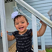 Brittany is registered to the contest to win money with this photo: toddler, child, smiling, happy, portrait, outdoor, porch, house, railing, stairs, wooden_deck, flower_headband, black_clothing, earrings, short_hair, standing, laughter, playful, blue_siding, daylight