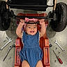 baby, child, smiling, blue_outfit, pink_headband, mechanics_creeper, tools, wrench, screwdriver, stroller, wheels, floor, concrete, hands, legs, cute, happy, indoor, person, repair