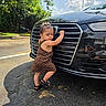 black_car, car, child, curious, cute, daytime, dress, footwear, greenery, grille, outdoor, parking_lot, pavement, polka_dot, reflection, shadow, sunlight, toddler, trees, young_child