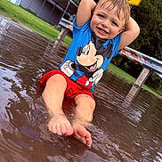 Kingston is registered to the contest to win money with this photo: child, toddler, puddle, water, barefoot, mickey_mouse, tshirt, red_shorts, smiling, outdoor, grass, road_sign, playful, wet_hair, sitting, summer, fun, nature, daylight, happy
