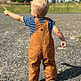 Hank is registered to the contest to win money with this photo: toddler, child, blonde_hair, overalls, pointing, outdoor, gravel, footwear, short_sleeve_shirt, nature, daylight, rural, background, house, tree, sky, person, back_view, casual_clothing, sunlight