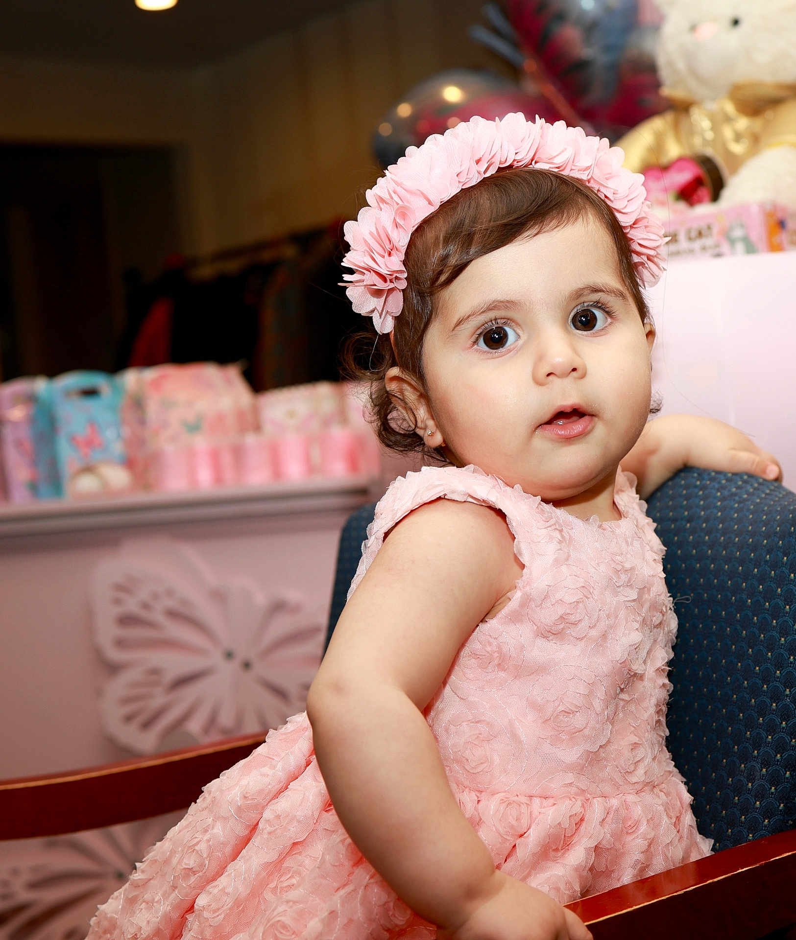 Mariana is registered to the contest to win money with this photo: baby, celebration, chair, child, closeup, curly_hair, cute, decorations, expression, furniture, happy, headband, indoor, party, pink_dress, plush_toy, portrait, seated, soft_lighting, toddler