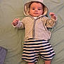 baby, infant, child, hoodie, striped_clothing, shorts, socks, bed, blanket, floor_tiles, person, indoors, cute, laying_down, looking_at_camera, young, small, comfortable, casual_clothing, resting