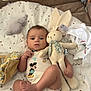 baby, infant, plush_toy, rabbit, blanket, couch, clothing, onesie, foot, hand, soft_toy, pattern, cute, indoors, child, lying_down, fabric, stuffed_animal, comfort, relaxed