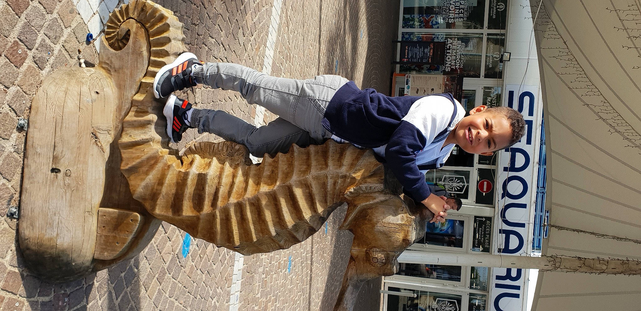 Léandre participe au concours pour gagner de l'argent avec cette photo : arm, boot, eyewear, fun, fur, glove, head, joy, pedestrian, person, sitting, smile, street, street_fashion, street_performance, tree, wood