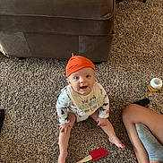Oliver is registered to the contest to win money with this photo: baby, orange_hat, bib, carpet, sitting, smiling, diaper, spatula, couch, floor, person, sock, leg, toy, indoor, child, happy, home, clothing, furniture