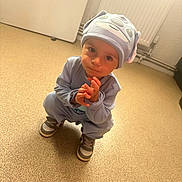 Mattoe joined the competition — help win amazing prizes! toddler, child, blue_outfit, hat, sneakers, indoor, floor, radiator, door, curious, squatting, playful, young_child, person, casual_clothing, looking_up, hands, headwear, expression, warm_lighting