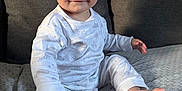 Diego joined the competition — help win amazing prizes! baby, child, pajamas, white_clothing, remote_control, couch, gray_couch, smile, sitting, indoor, face, happy, foot, hand, furniture, child_playing, home, infant, person, cozy