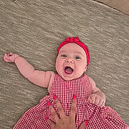 Elma participe au concours pour gagner de l'argent avec cette photo : baby, child, smiling, red_headband, red_dress, checkered_pattern, hand, carpet, texture, happy, cute, infant, lying_down, playful, person, skin, fingers, nail_polish, home, indoors