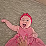 baby, child, smiling, red_headband, red_dress, checkered_pattern, hand, carpet, texture, happy, cute, infant, lying_down, playful, person, skin, fingers, nail_polish, home, indoors