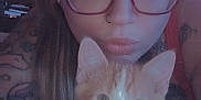 Butters is registered to the contest to win money with this photo: woman, glasses, tattoo, cat, kitten, orange_and_white, collar, bell, face, closeup, selfie, indoor, heart_shape, pet, cute, animal, young_adult, expression, portrait, curious
