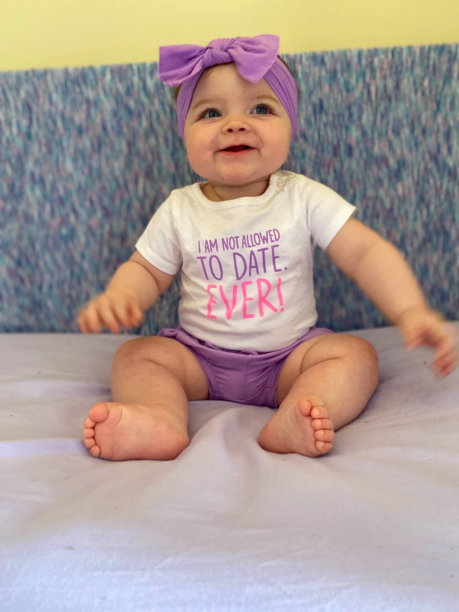 Mariyah is registered to the contest to win money with this photo: baby, baby_bloomers, baby_products, baby_toddler_clothing, cheek, child, facial_expression, hair_accessory, head, headgear, headwear, joy, person, pink, product, purple, sitting, skin, sleeve, smile