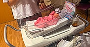 China joined the competition — help win amazing prizes! baby, bassinet, bracelet, cup, hat, hospital, hospital_room, indoor, medical_equipment, newborn, parent, person, phone, pink_clothing, portrait, purple_chair, swaddled, table, white_shirt, wooden_floor