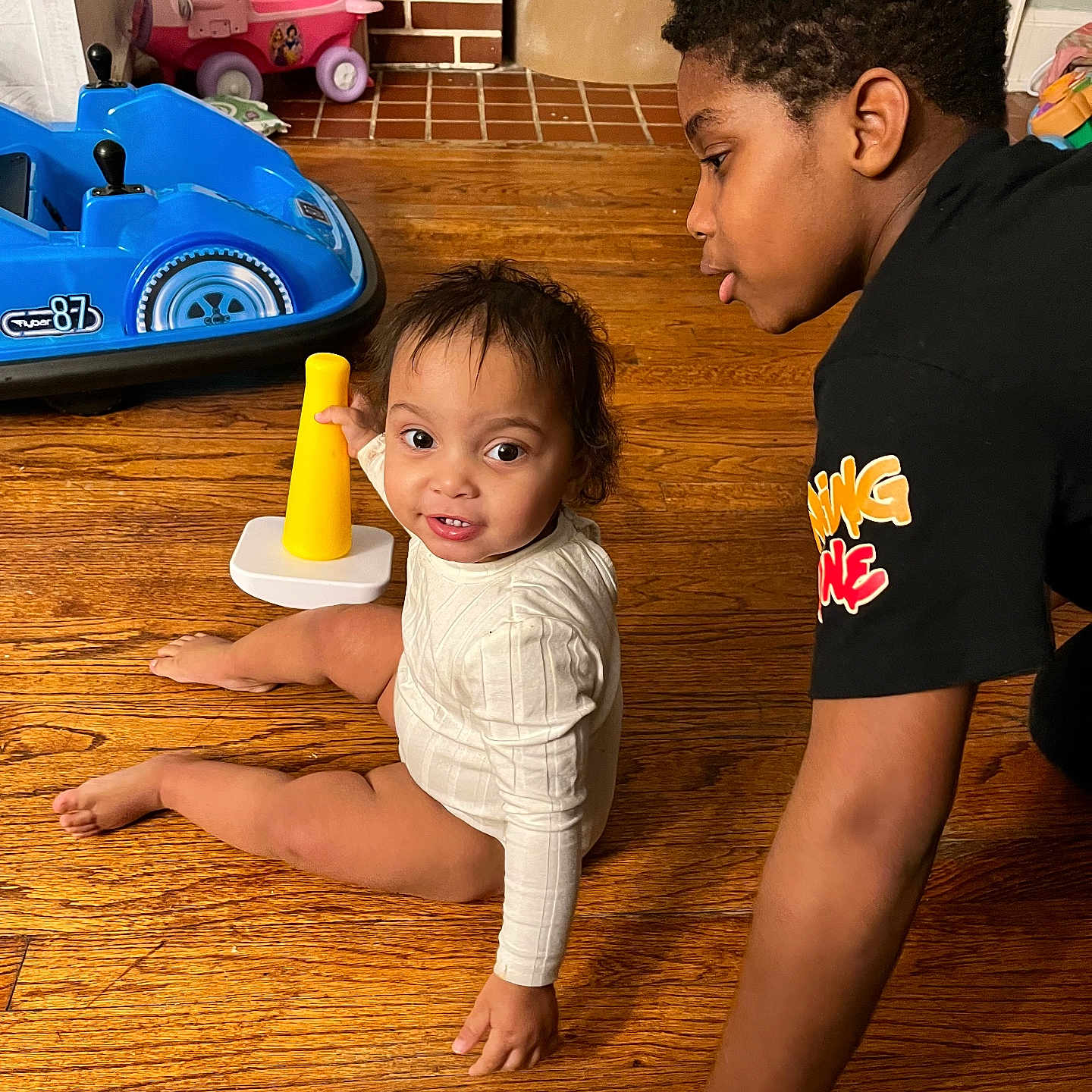 Anila joined the competition — help win amazing prizes! baby, black_tshirt, brick_wall, candid, car_toy, child, curly_hair, floor, home, indoor, infant, interaction, pink_toy, play, shirt, sitting, toy, wooden_floor, yellow_toy, young_boy