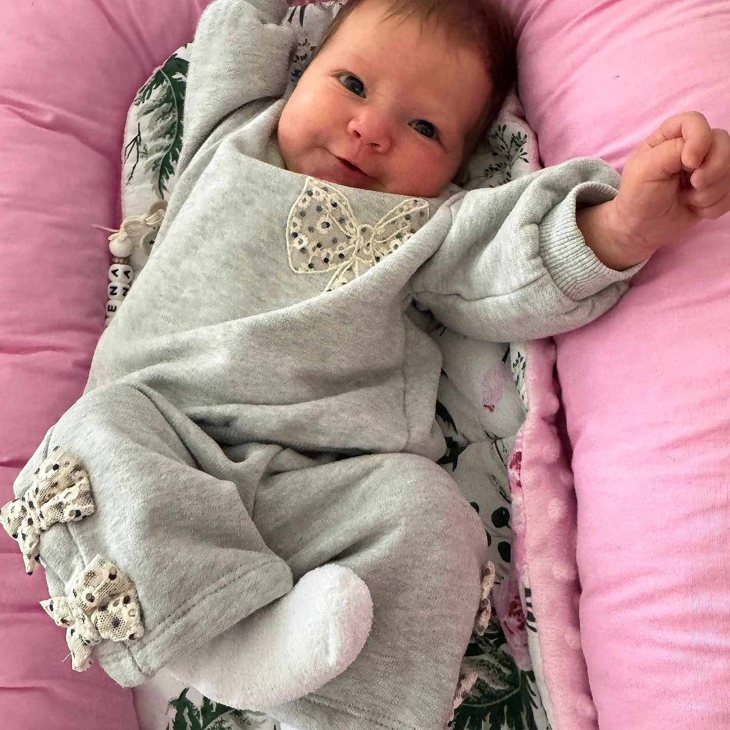 Lena is registered to the contest to win money with this photo: arms, baby, blanket, bows, child, cozy, cute, face, grey_outfit, happy, indoors, infant, legs, lying_down, pink_cushion, portrait, smiling, soft, white_socks, young