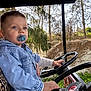 child, toddler, pacifier, denim_jacket, striped_pants, steering_wheel, vehicle, outdoor, trees, greenery, curious, blue_eyes, person, casual_clothing, daylight, nature, hand, portrait, seat, young_child