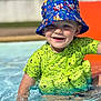 child, toddler, smiling, pool, water, splashing, hat, bucket_hat, blue, green_shirt, dinosaur_print, sunlight, outdoor, happy, summer, play, cute, face, person, fun