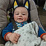baby, baby_chair, blanket, blue_clothing, child, comfort, cute, ears, face, floor, hand, headband, indoor, infant, person_in_background, portrait, seatbelt, smiling, stars_pattern, striped_pajamas