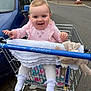 baby, blanket, car, casual, child, cute, daylight, happy, infant, outdoor, parking_lot, person, pink_clothing, plush_toy, retail, shopping_trolley, smiling, storefront, toddler, white_sock