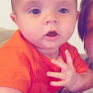 Westley is registered to the contest to win money with this photo: baby, child, infant, face, eyes, mouth, hand, orange_shirt, skin, person, curious, closeup, candid, indoor, casual, expression, young, resting, holding, portrait