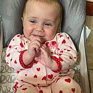 Ainsley is registered to the contest to win money with this photo: baby, child, infant, onesie, heart_pattern, smiling, happy, seated, baby_chair, indoor, cute, hands, face, blue_eyes, pink_clothing, soft_fabric, adorable, cozy, playful, young