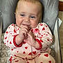 adorable, baby, baby_chair, blue_eyes, child, cozy, cute, face, hands, happy, heart_pattern, indoor, infant, onesie, pink_clothing, playful, seated, smiling, soft_fabric, young