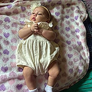 Allison joined the competition — help win amazing prizes! baby, infant, blanket, hearts, white_outfit, headband, flower, socks, lying_down, soft_texture, cute, child, portrait, indoors, cloth, hands, legs, pink, purple, sleepwear