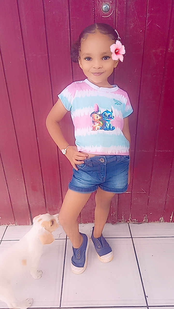 Géna a rejoint le concours — aidez-le/la à gagner de superbes lots ! child, girl, puppy, dog, flower, tshirt, shorts, shoes, hand_on_hip, pose, standing, outdoor, door, red_door, tile_floor, bracelet, smile, curly_hair, cute, casual_clothing