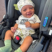 Kairo joined the competition — help win amazing prizes! baby, smiling, car_seat, dinosaur_hat, green_socks, shorts, tshirt, infant, cute, child, seatbelt, happy, indoors, cloth, headwear, person, sitting, young_child, car, safety