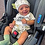 baby, smiling, car_seat, dinosaur_hat, green_socks, shorts, tshirt, infant, cute, child, seatbelt, happy, indoors, cloth, headwear, person, sitting, young_child, car, safety