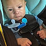 baby, car_seat, pacifier, infant, child, blue_clothing, black_harness, straps, safety, seat_belt, closeup, cute, serious_expression, hands, indoor, portrait, young_child, seat, child_safety, infant_seat