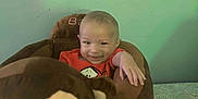 Adan is registered to the contest to win money with this photo: baby, child, plush_toy, stuffed_animal, monkey, baby_seat, smiling, red_clothing, indoor, green_wall, striped_pillow, cute, happy, infant, person, soft_toy, toddler, face, hand, foot
